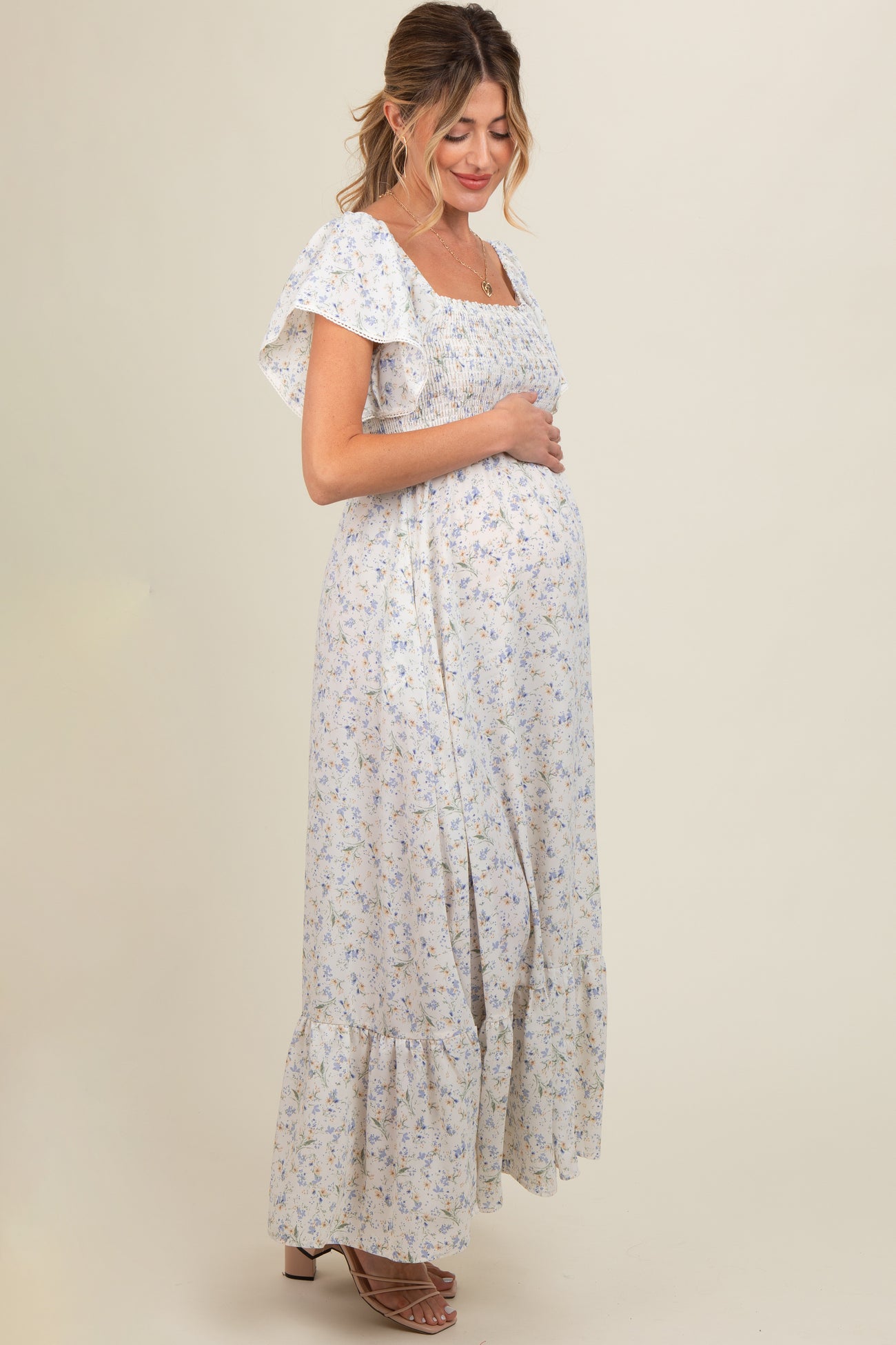 woman wearing a light purple floral maternity maxi dress, gently cradling her baby bump