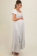 woman wearing a light purple floral maternity maxi dress, gently cradling her baby bump