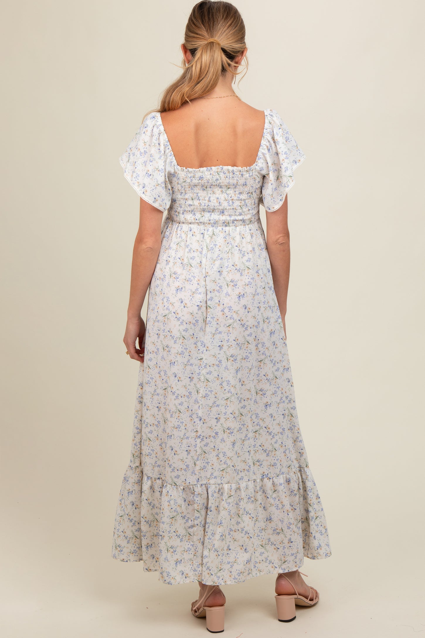 woman wearing a floral print maternity maxi dress with a smocked bodice and ruffle sleeves, showing a baby bump