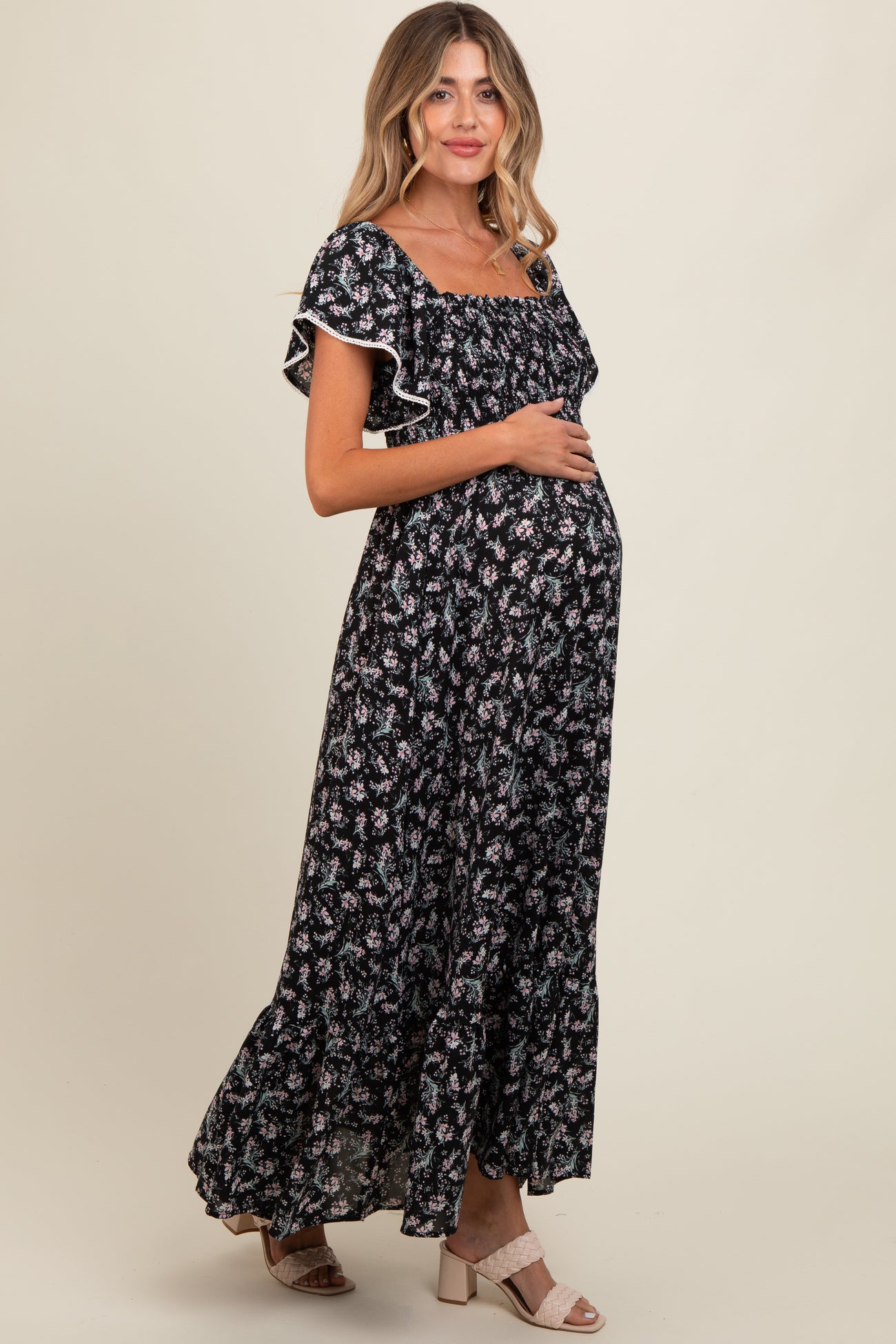 woman wearing a black floral maternity maxi dress with ruffled sleeves and holding her baby bump