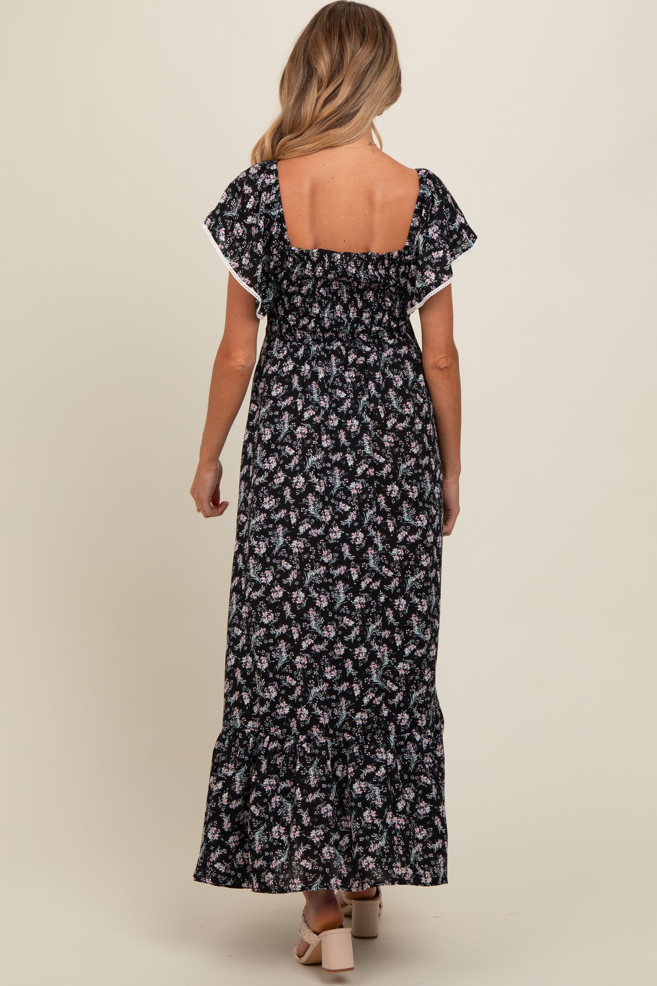 woman wearing a black floral print maternity maxi dress with flutter sleeves and a ruffled hem, seen from the back