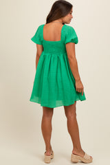 woman wearing a green smocked maternity dress with short sleeves and a square neckline, standing with her back to the camera