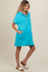 woman wearing a bright turquoise maternity polo dress with pockets and short sleeves, showing her baby bump