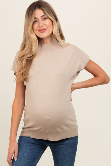 woman wearing a beige short sleeve maternity top, showing her baby bump, paired with blue jeans