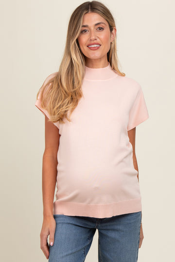 woman wearing a light pink short sleeve maternity top and showing her baby bump