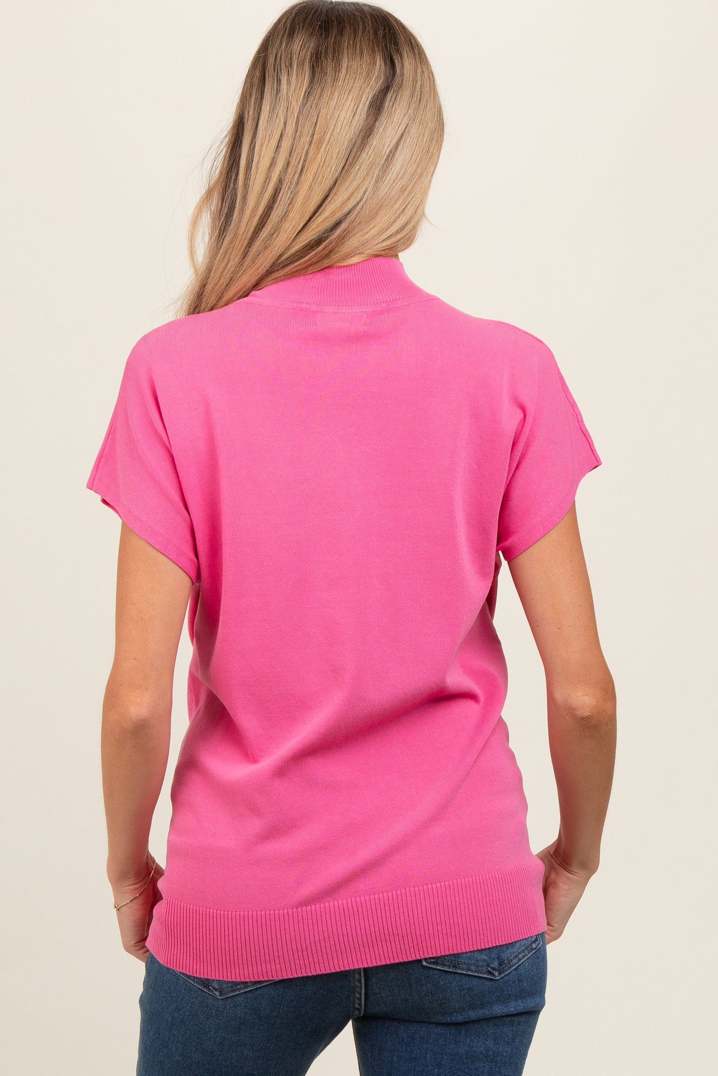 woman wearing a pink short sleeve maternity top, view from the back, styled with blue jeans