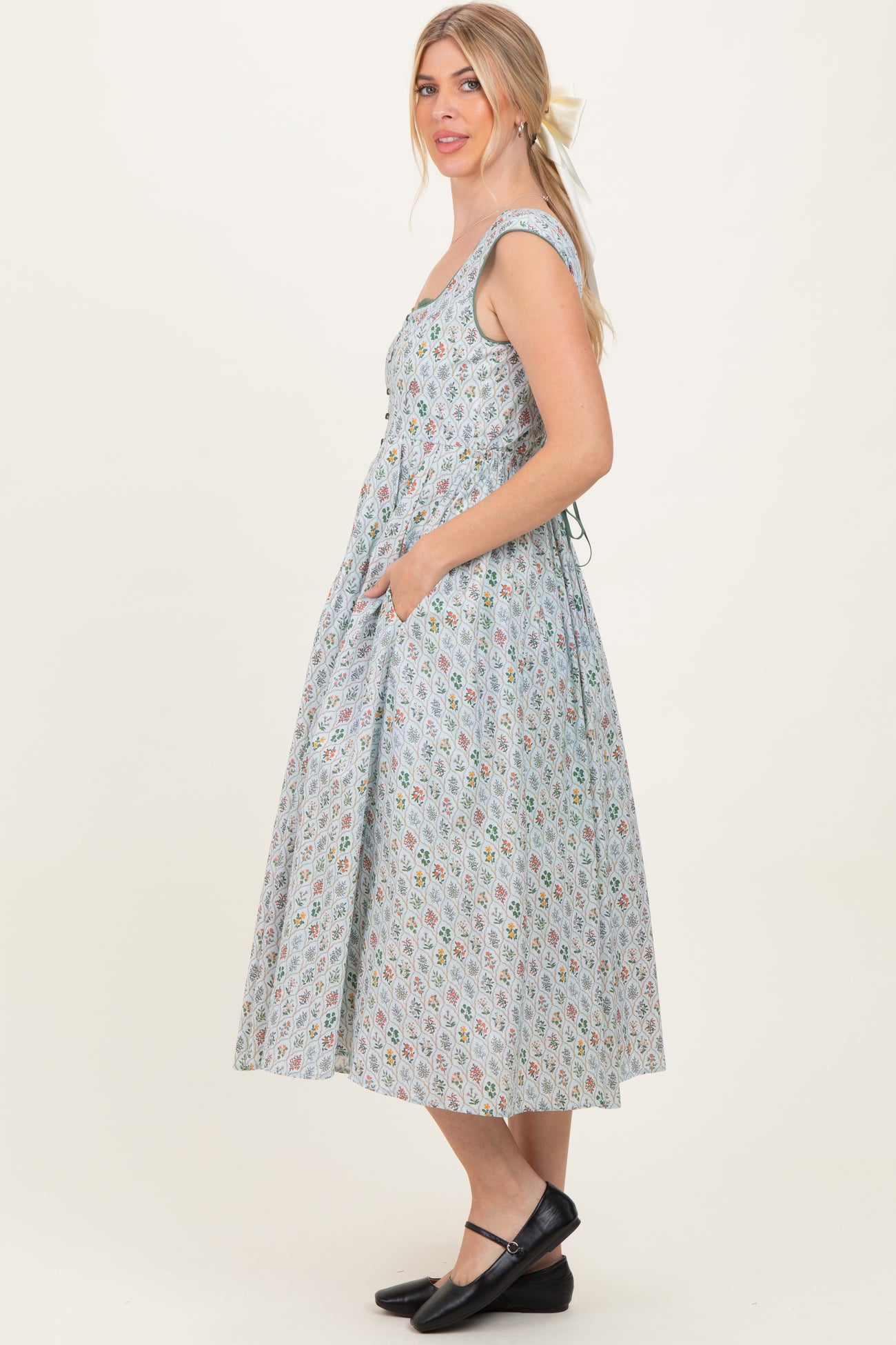 woman wearing a sleeveless light blue floral midi dress with pockets and a fitted bodice