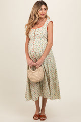 woman wearing a floral print maternity dress with cap sleeves, holding a woven bag and showing her baby bump