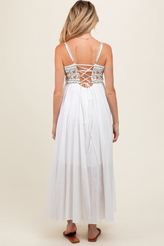woman wearing a white maternity maxi dress with a floral embroidered back and lace-up detail