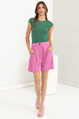 woman wearing a green cap sleeve top, pink high-waisted shorts, and patterned sheer tights with pink heels