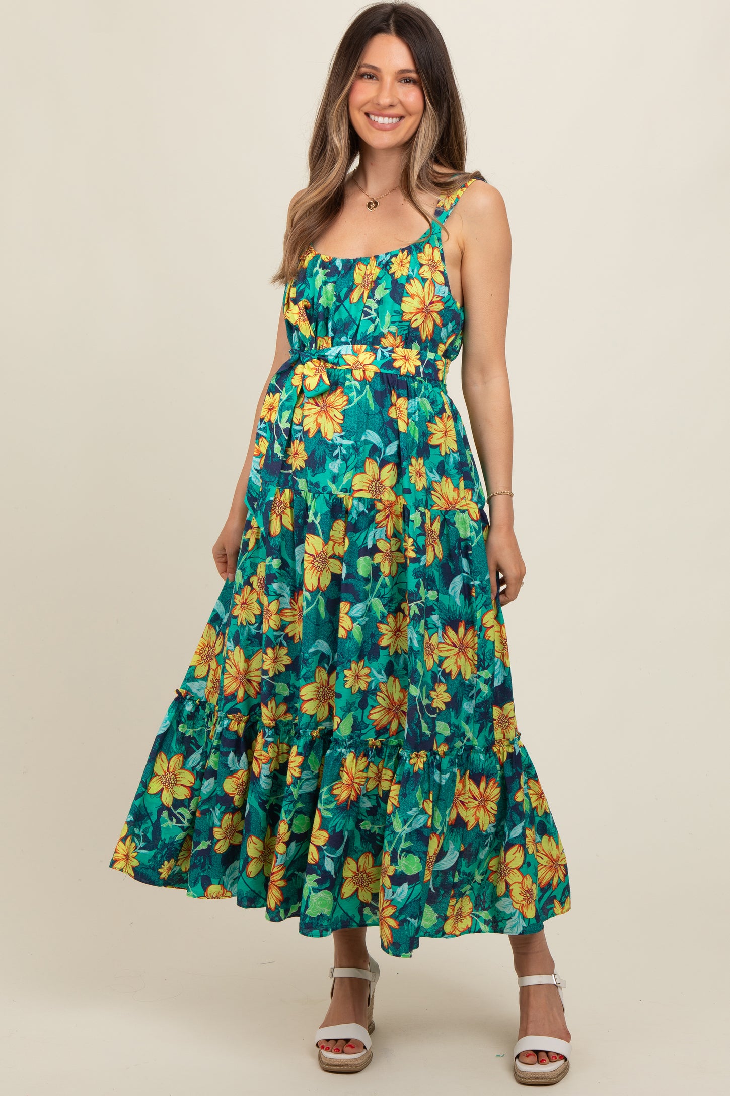 woman wearing a floral print maternity dress in teal and yellow with a ruffled hem and spaghetti straps, baby bump visible