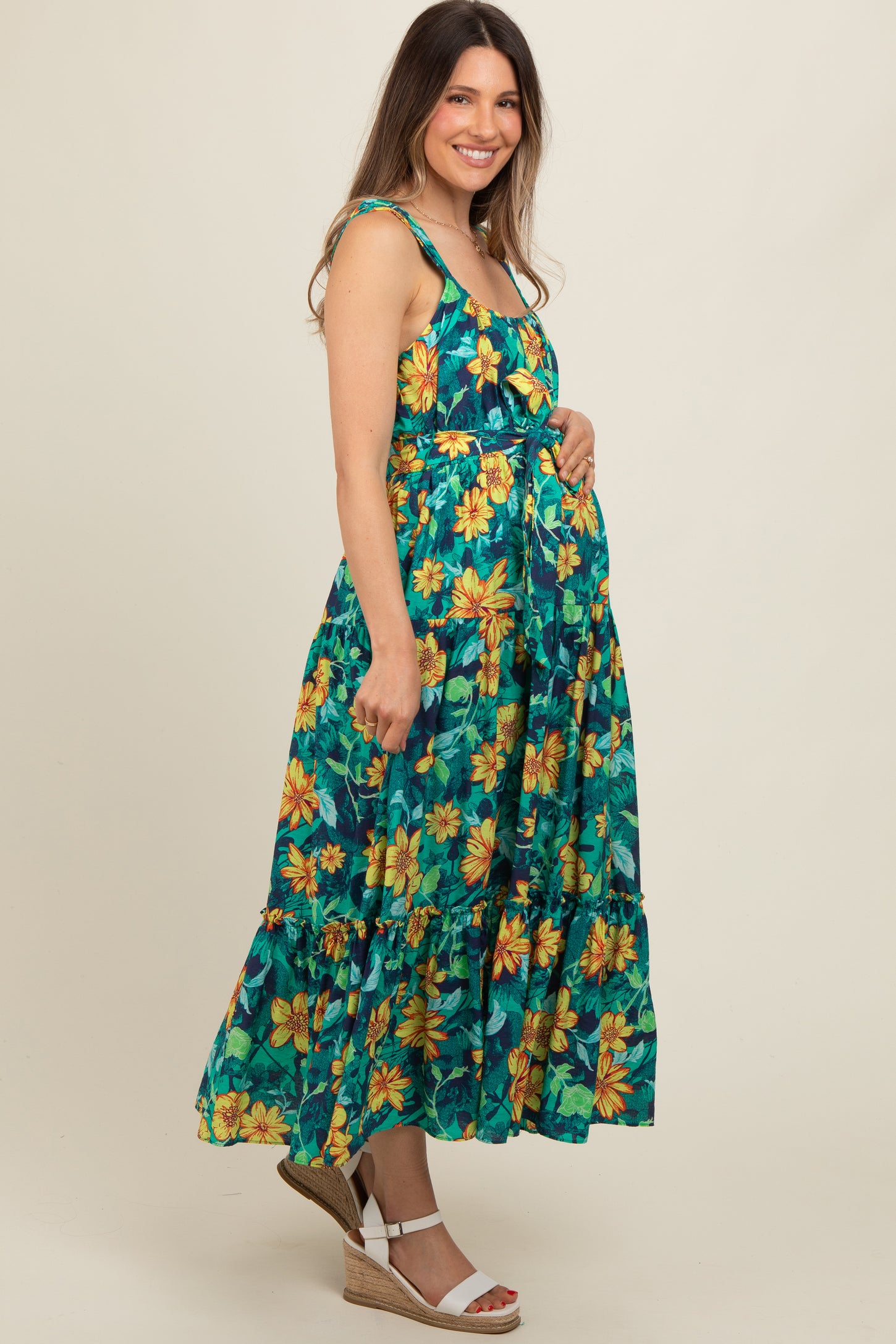 woman wearing a green floral maternity maxi dress with a fitted bodice and tiered skirt, cradling her baby bump