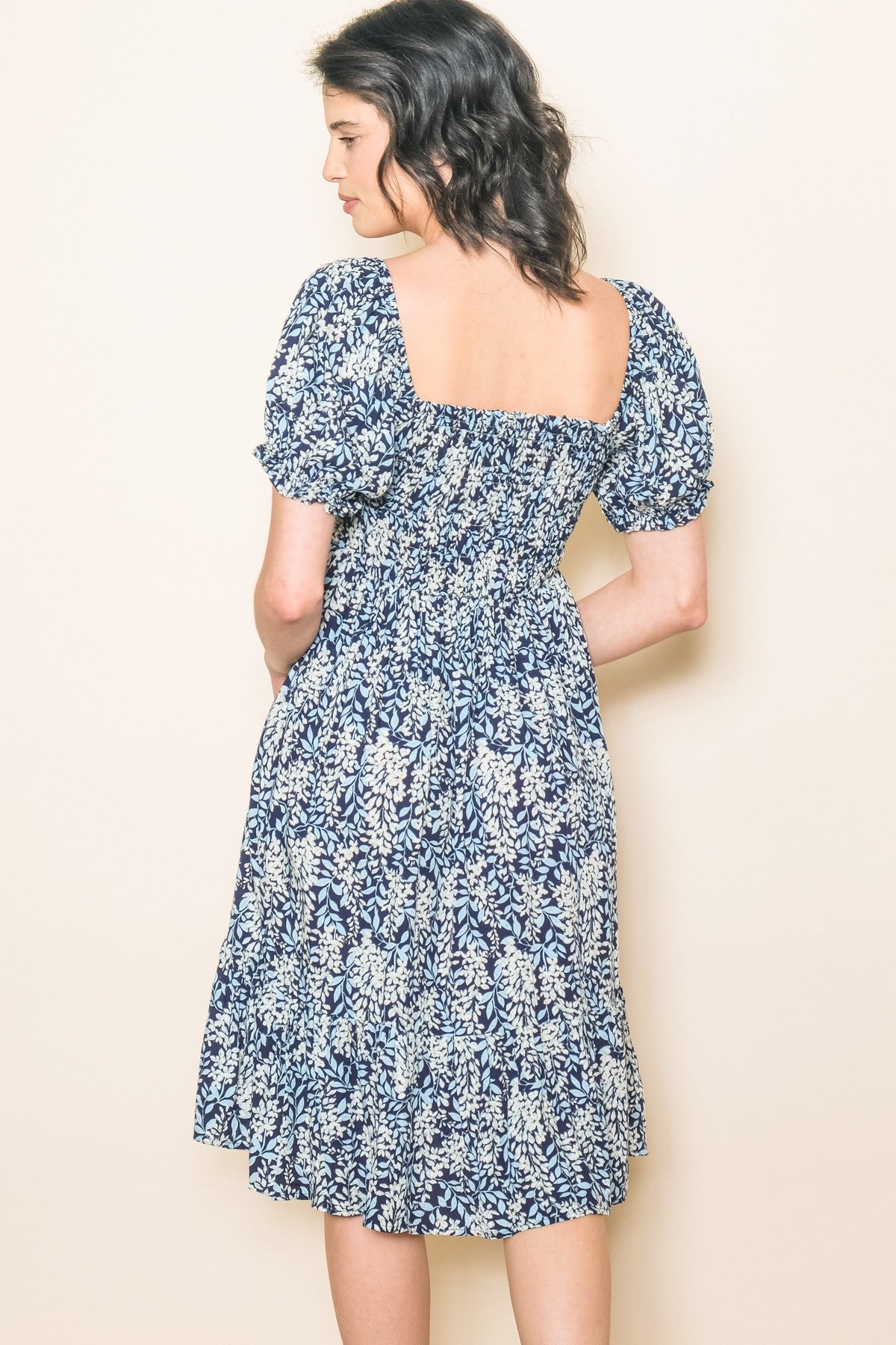 woman wearing a navy floral puff sleeve dress with a smocked bodice and tiered skirt, viewed from the back