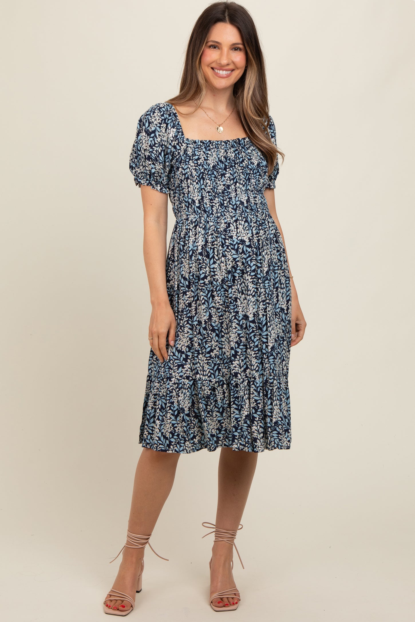 woman wearing a navy floral maternity dress with a square neckline and puff sleeves, showing her baby bump