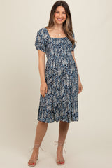 woman wearing a navy floral maternity dress with a square neckline and puff sleeves, showing her baby bump