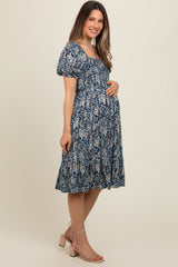 woman wearing a navy blue floral maternity dress with puff sleeves and a tiered skirt, holding her baby bump