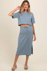 woman wearing a light blue maternity two-piece set with a cropped top and a midi skirt, featuring a side slit and drawstring waist