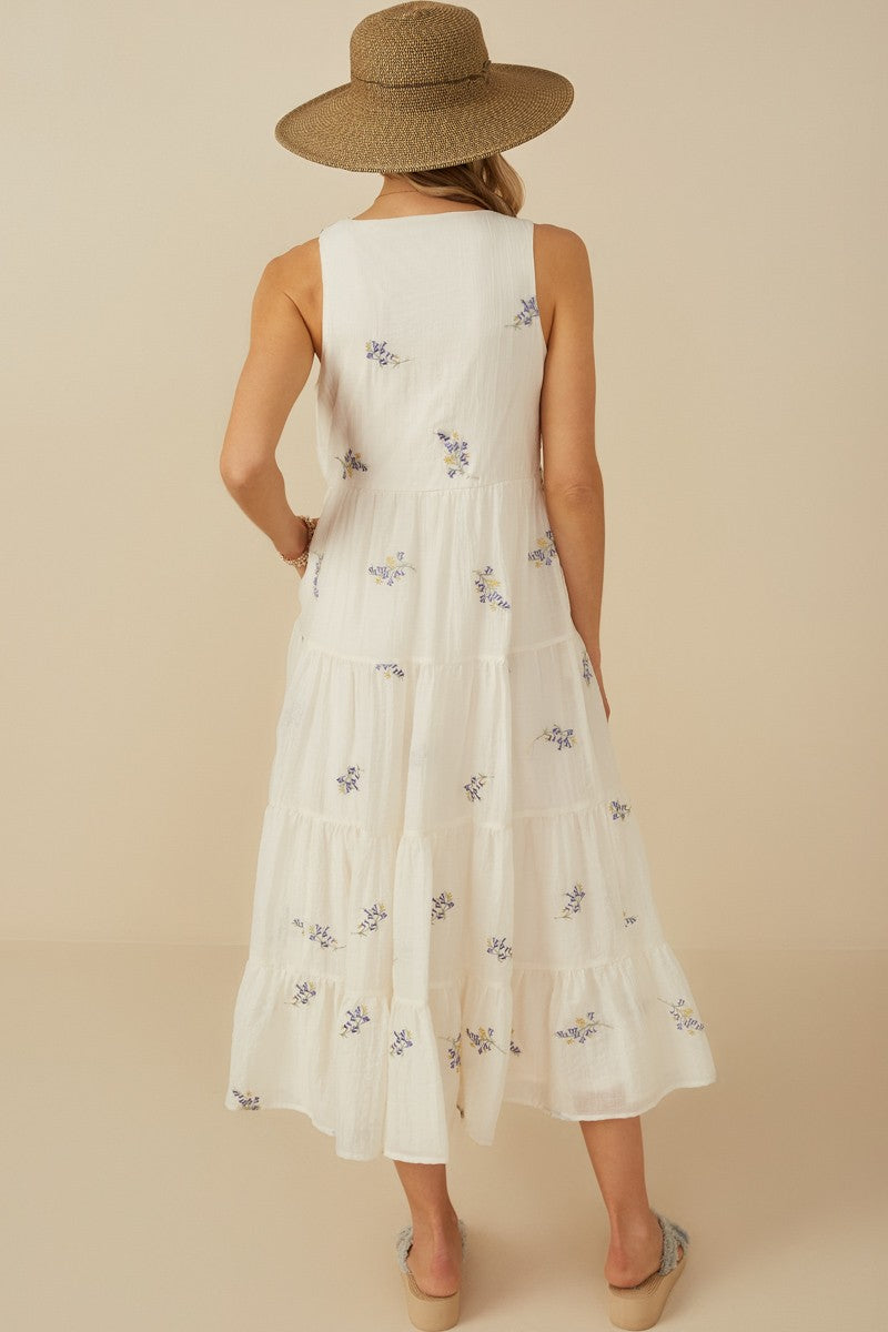 woman wearing a white floral embroidered maxi dress with a tiered design and a straw hat, showing the back view