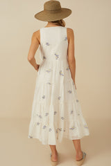 woman wearing a white floral embroidered maxi dress with a tiered design and a straw hat, showing the back view