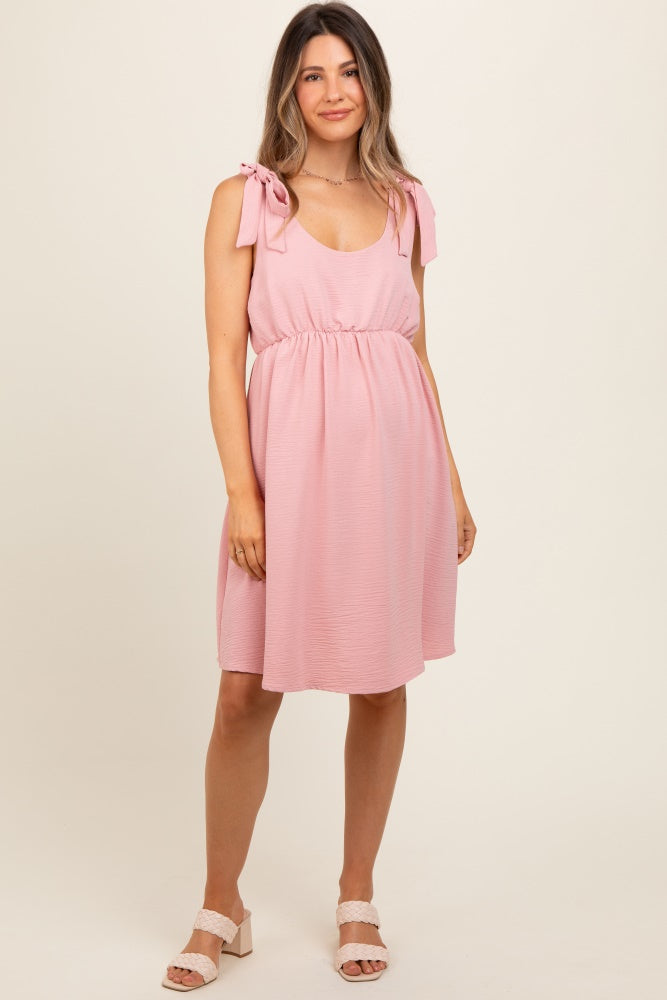woman wearing a light pink maternity dress with tie straps and an empire waist, featuring a relaxed fit