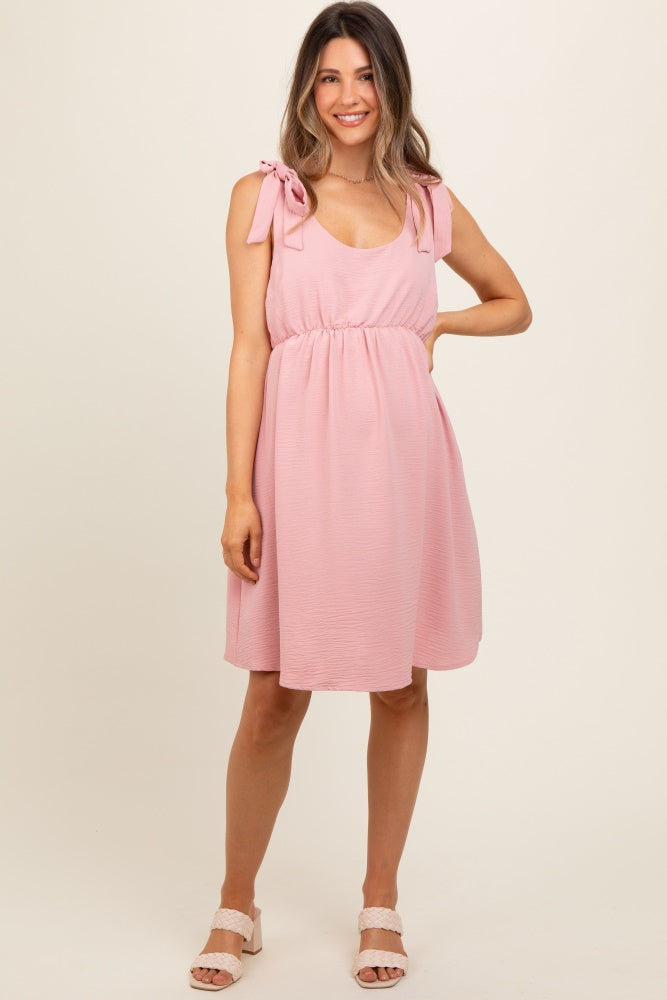 woman wearing a pink maternity dress with tie shoulder straps and an empire waist, showcasing her baby bump