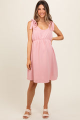 woman wearing a pink maternity dress with tie shoulder straps and an empire waist, showcasing her baby bump