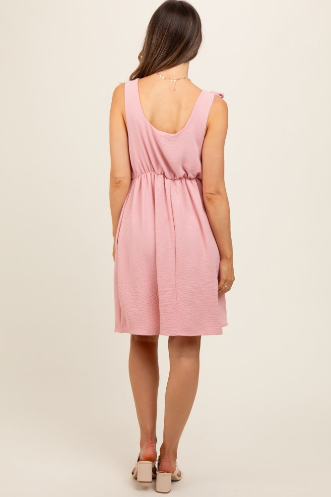 woman wearing a sleeveless pink maternity dress with a fitted waist and flared skirt, showing a relaxed fit from the back