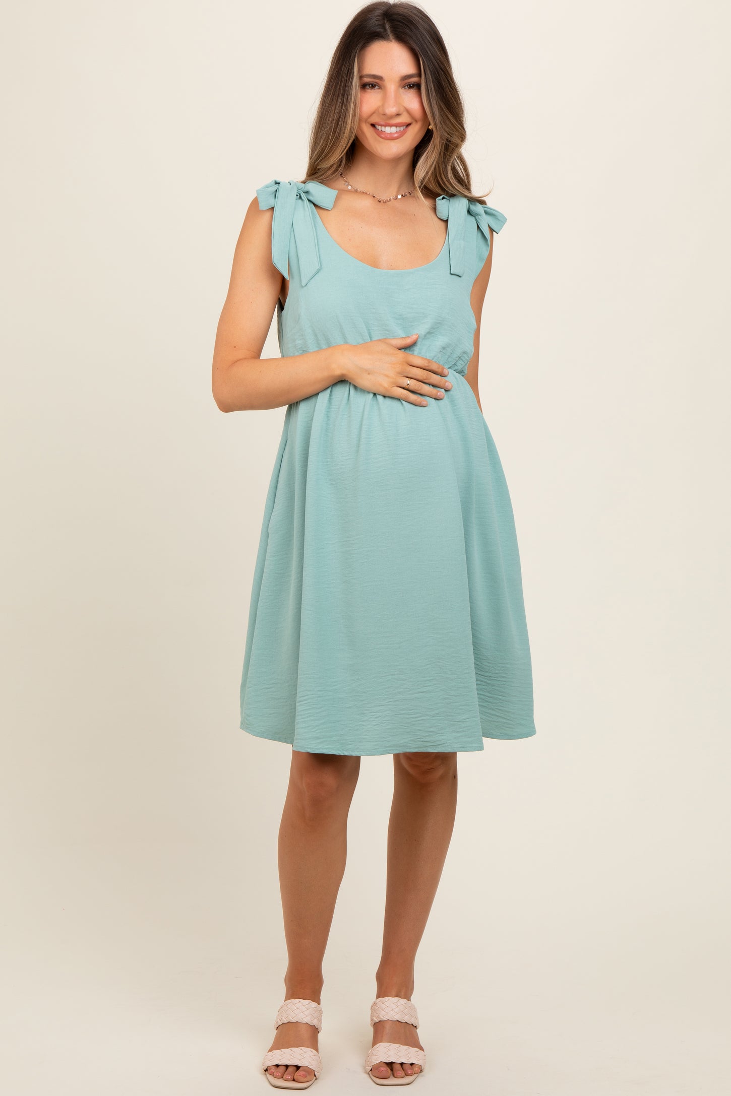 woman wearing a teal maternity dress with tie sleeves and holding her baby bump