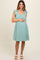 woman wearing a teal maternity dress with tie sleeves and holding her baby bump