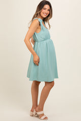 woman wearing a light teal maternity dress with tie shoulder straps and a visible baby bump