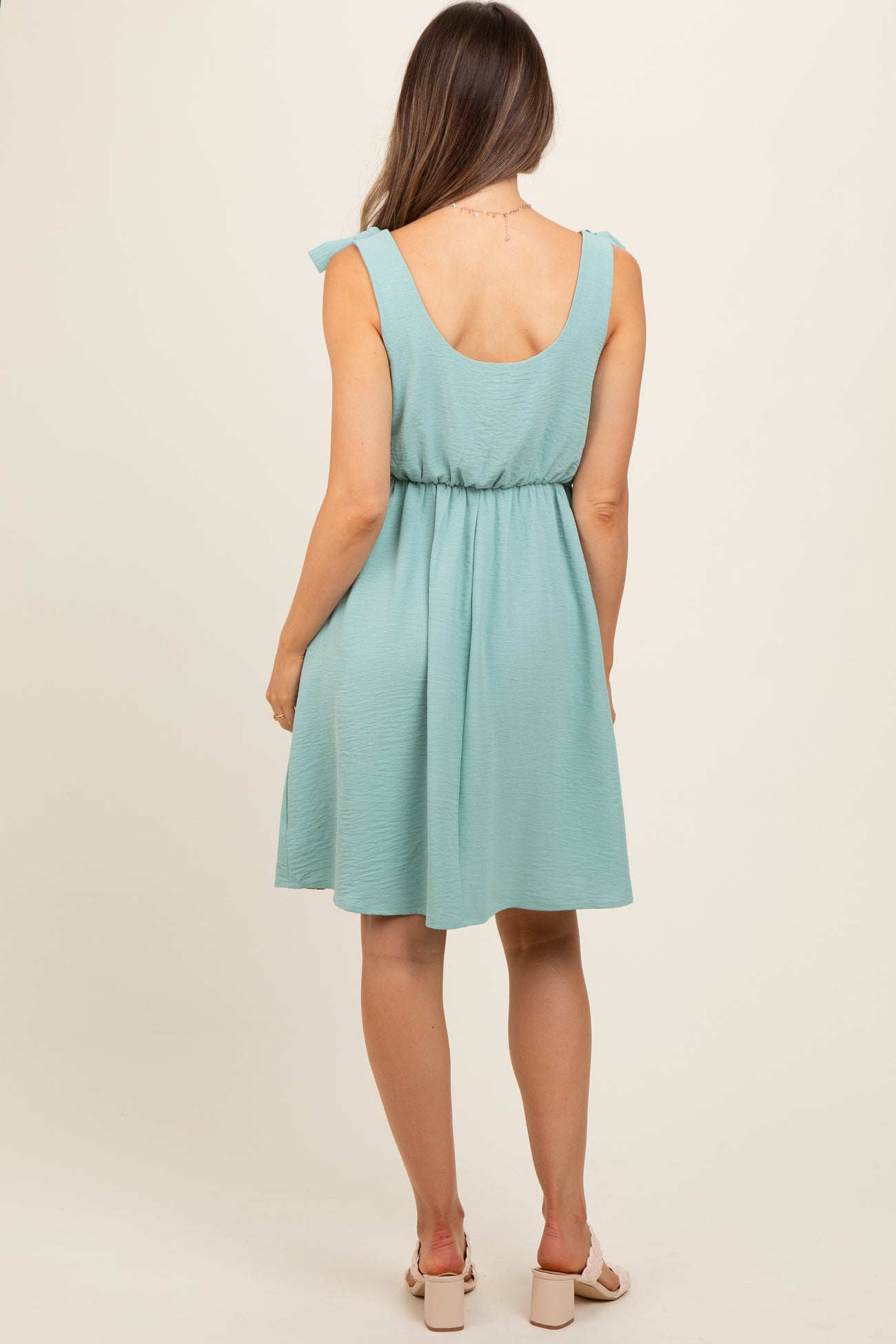 woman wearing a mint green maternity dress with a cinched waist and ruffled shoulder straps, shown from the back