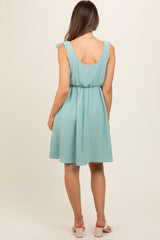 woman wearing a mint green maternity dress with a cinched waist and ruffled shoulder straps, shown from the back
