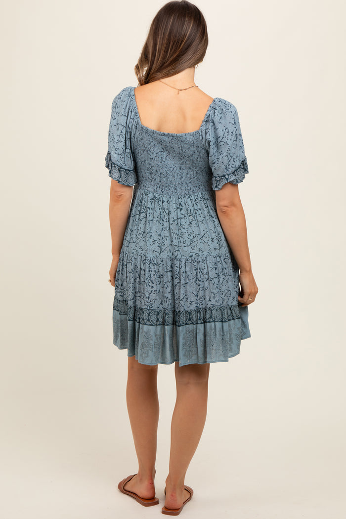 woman wearing a blue floral patterned maternity dress with puff sleeves and a smocked bodice, seen from the back