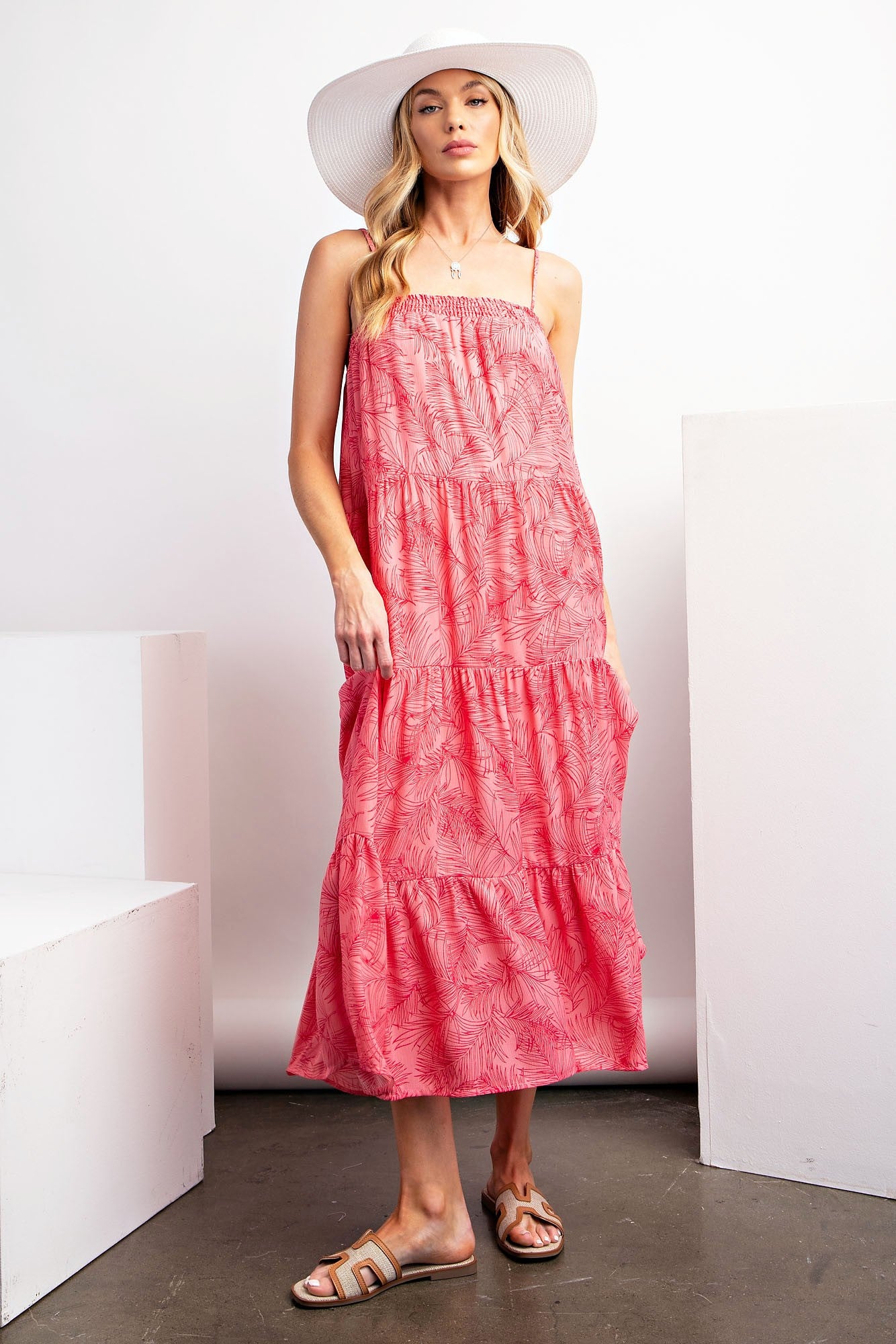 woman wearing a pink tropical print maxi dress with a tiered design and a wide-brimmed hat