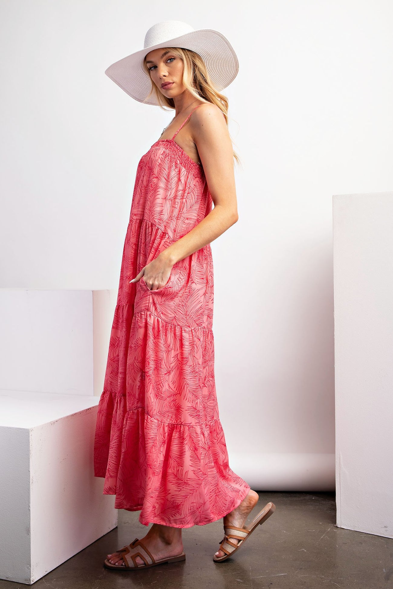 woman wearing a coral maxi dress with a tiered style and pockets, paired with a wide-brimmed white hat and sandals