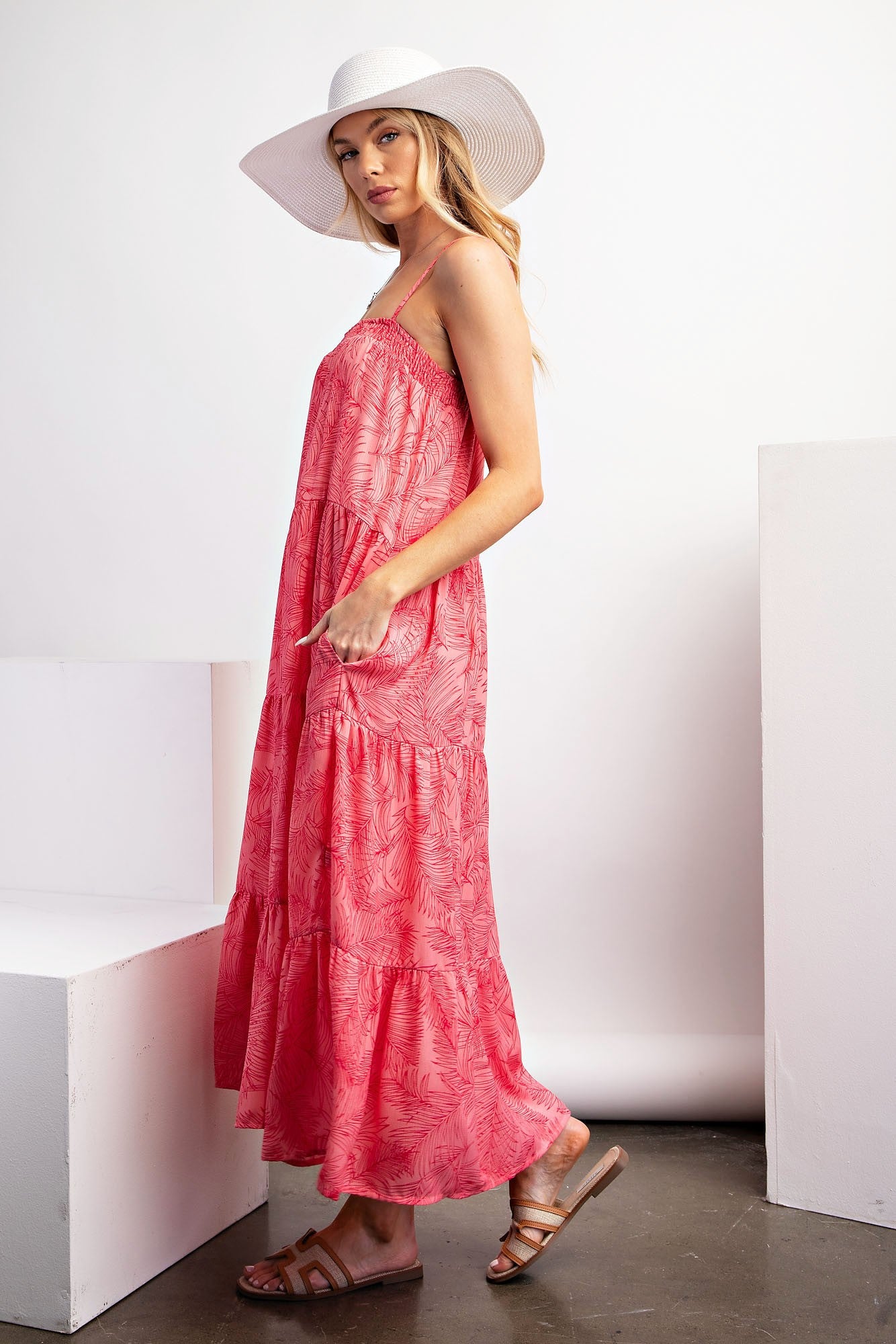 woman wearing a coral maxi dress with a tiered style and pockets, paired with a wide-brimmed white hat and sandals
