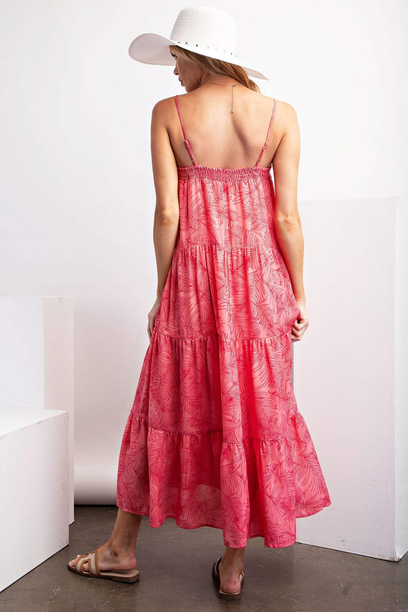 woman wearing a pink tiered maxi dress with a tropical pattern and spaghetti straps, showing the back view