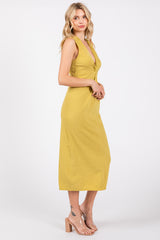 woman wearing a yellow sleeveless midi dress with a front twist detail, standing in profile against a plain background