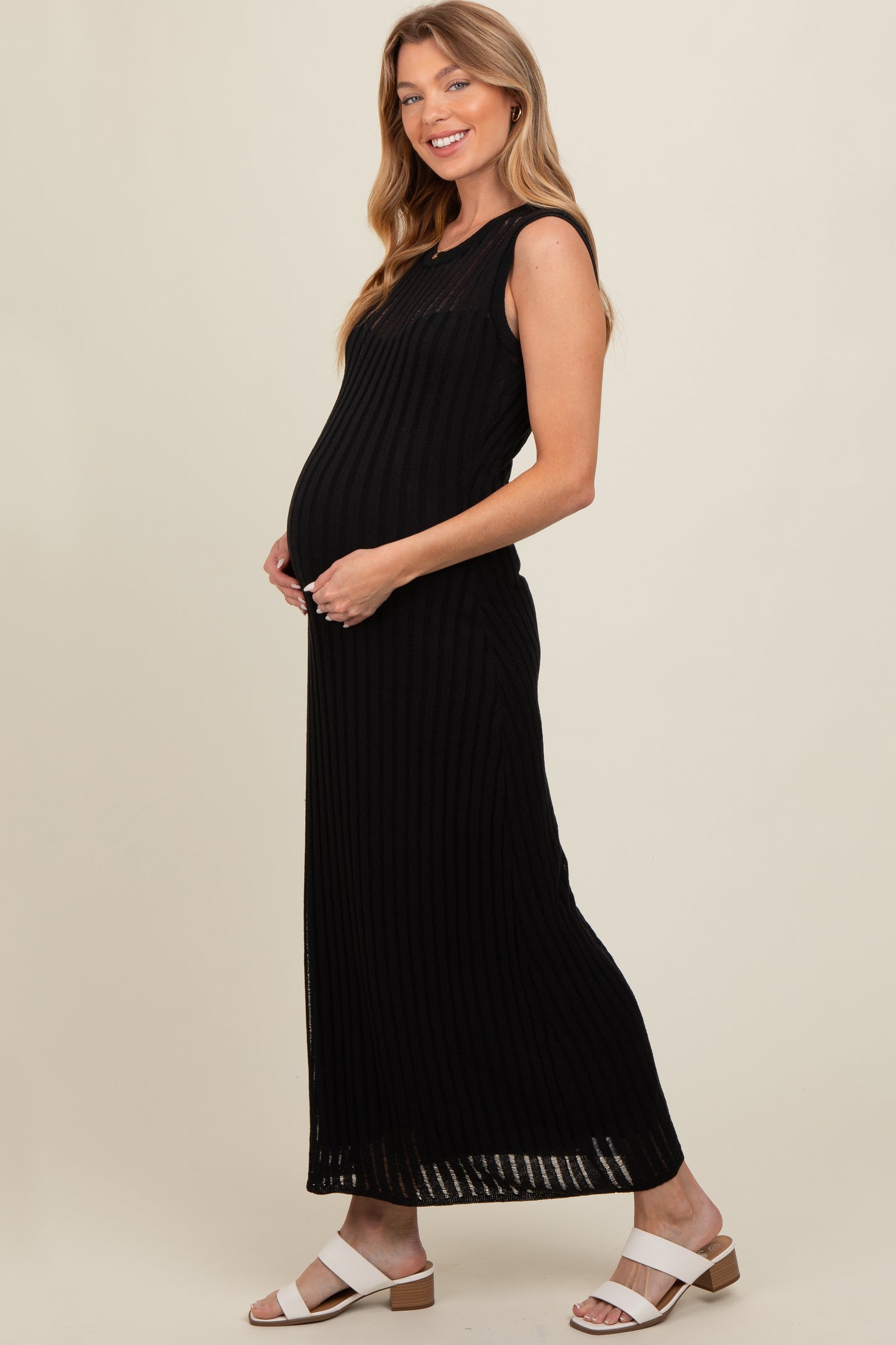 woman wearing a black ribbed maternity maxi dress and cradling her baby bump