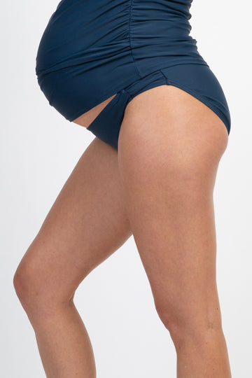 woman wearing a navy blue maternity swim bottom, featuring ruching and a snug fit around her baby bump