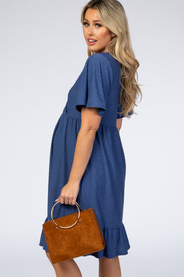 woman wearing a blue polka dot maternity dress with short sleeves and a ruffle hem, holding a brown handbag and showing her baby bump