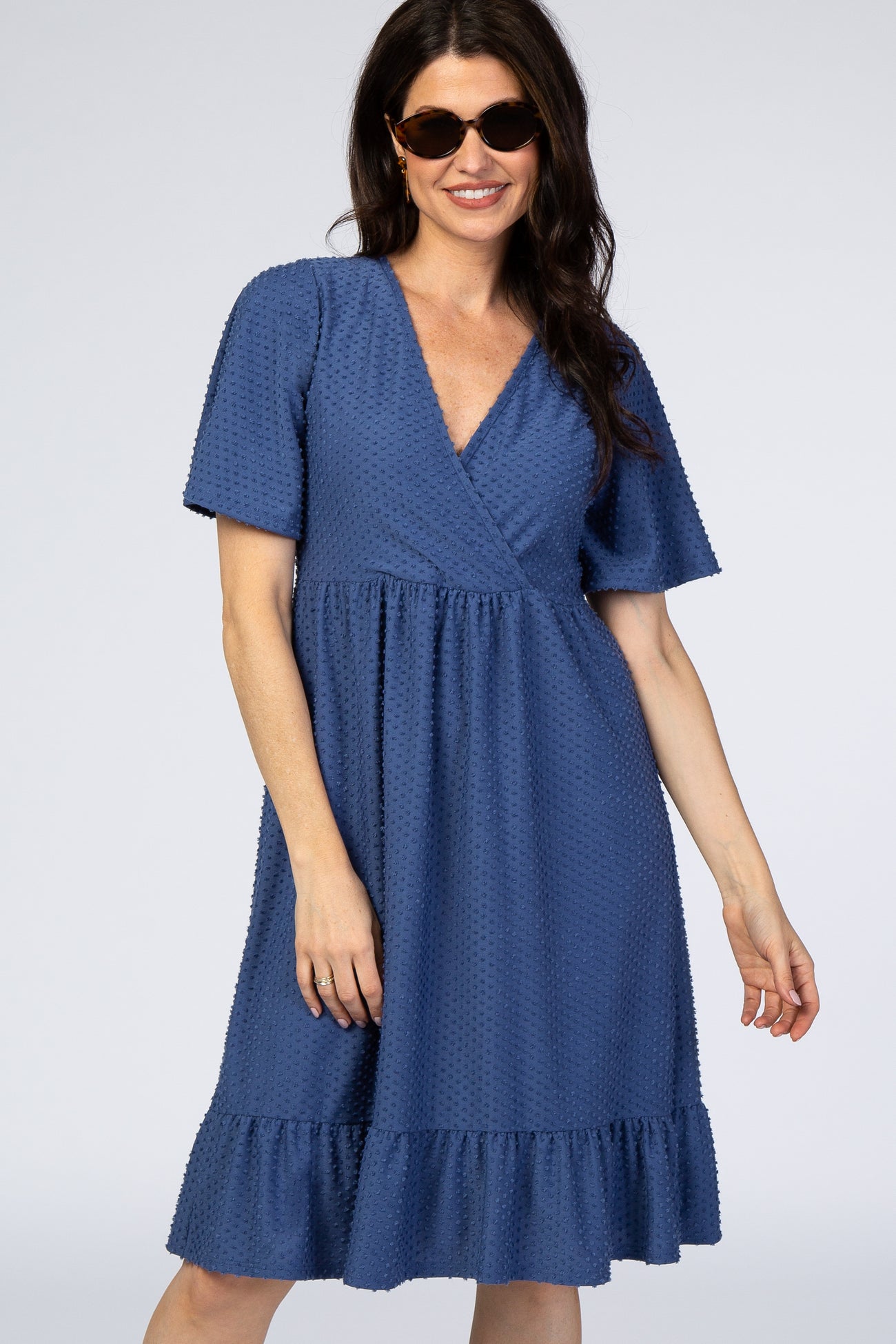 woman wearing a navy blue short sleeve dress with a deep V-neck and a ruffled hem, styled with sunglasses