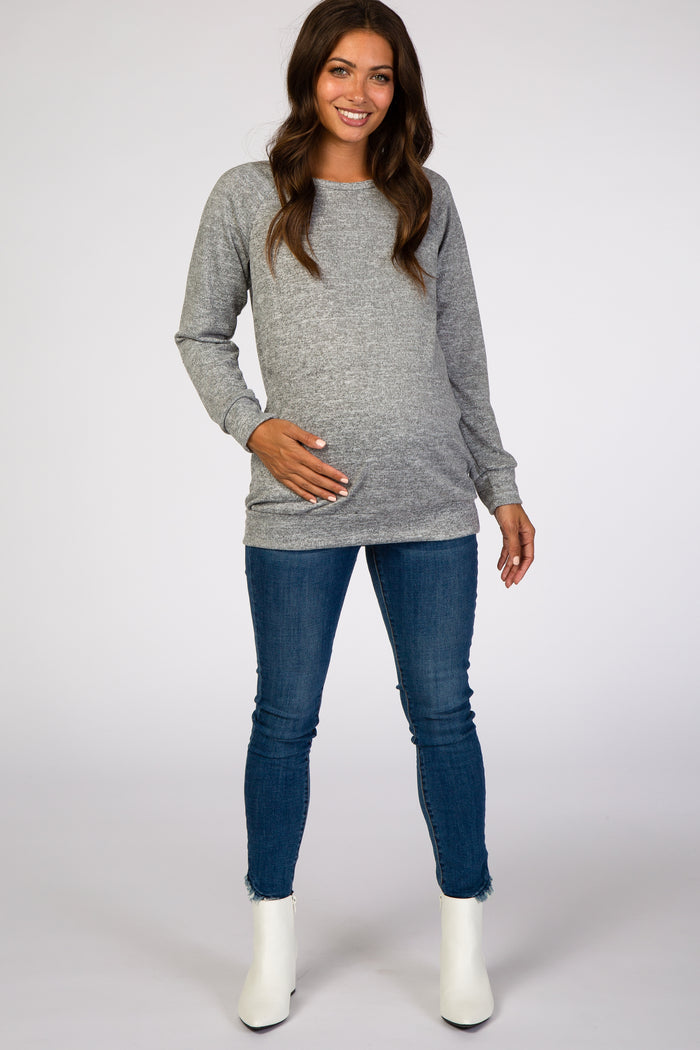 smiling pregnant woman wearing grey long sleeve maternity sweater and blue jeans with white boots