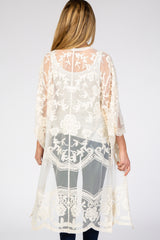 Back view of a woman wearing a cream floral lace sheer kimono cardigan over a white tank top and jeans