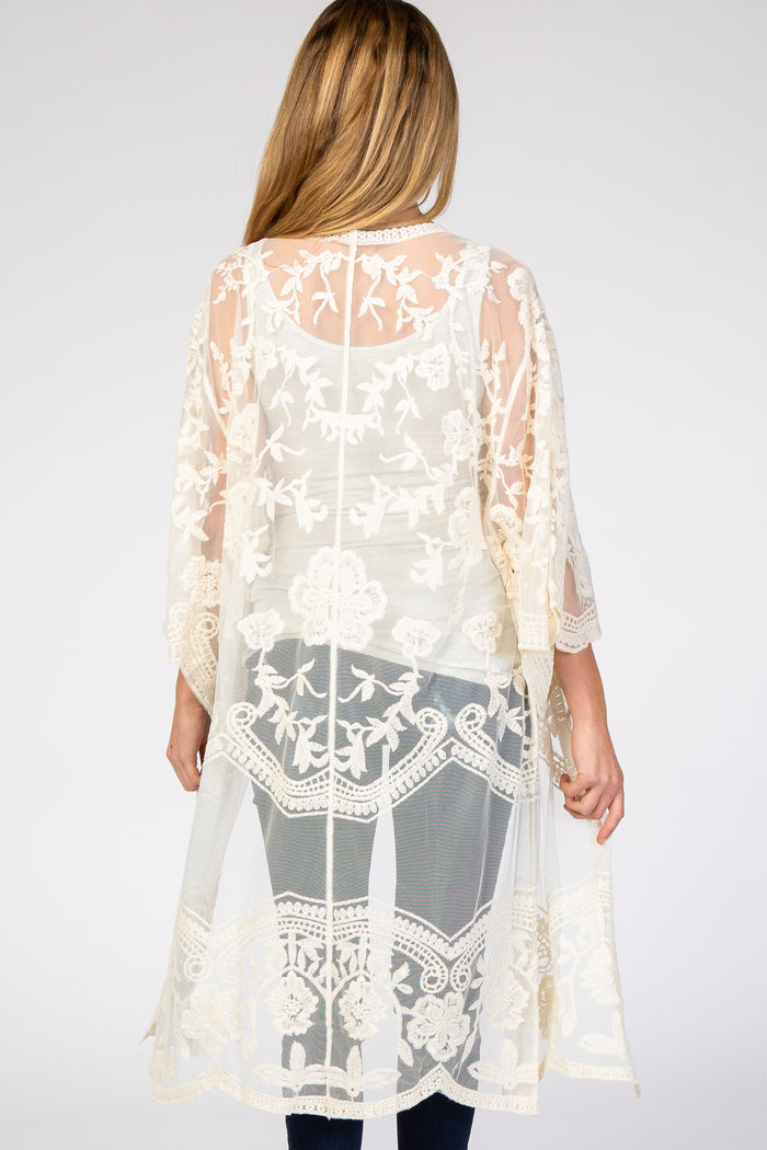 Back view of a woman wearing a cream floral lace sheer kimono cardigan over a white tank top and jeans