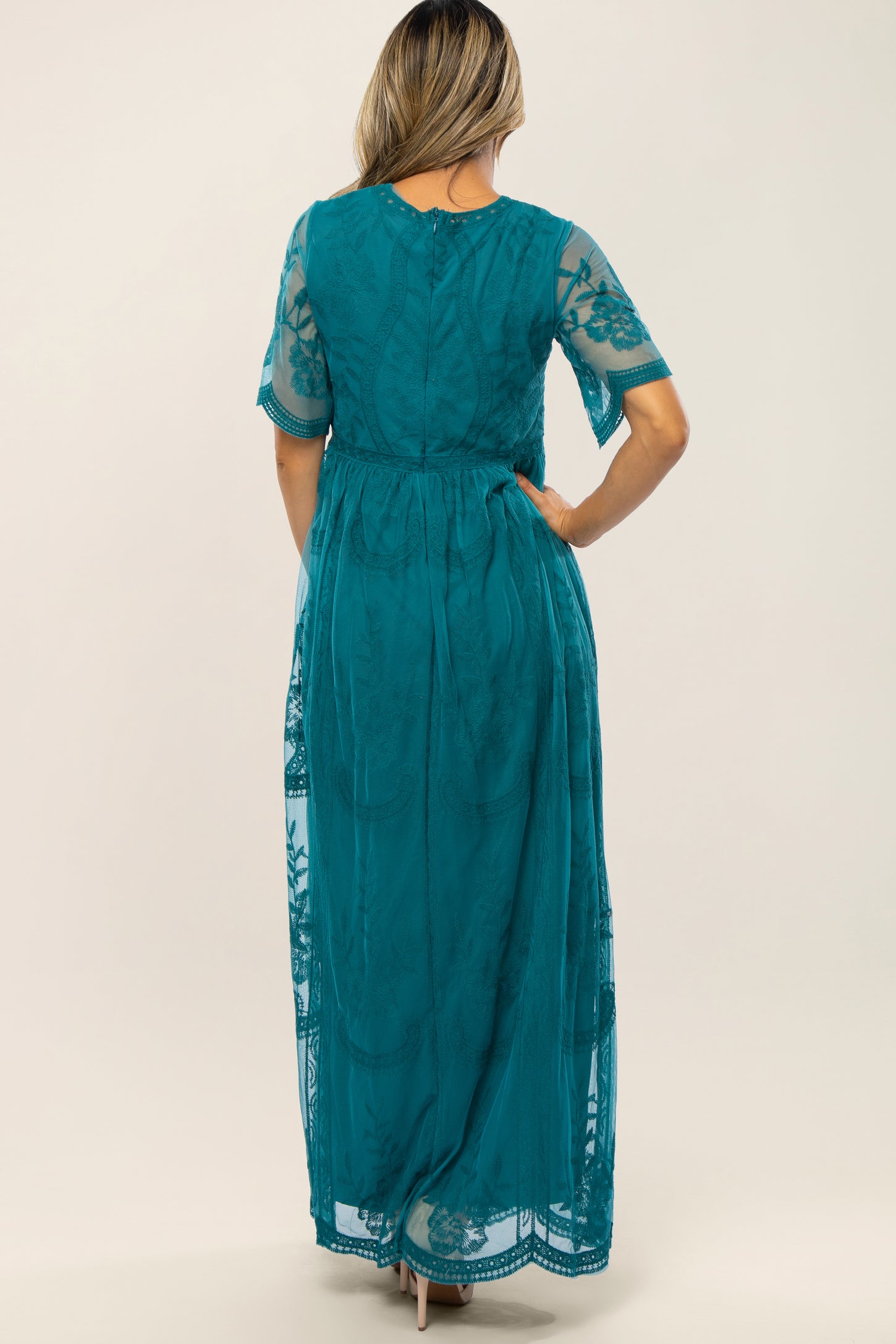 woman wearing a teal lace maxi dress with short sleeves and floral detailing, viewed from the back