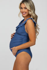 woman wearing a navy blue maternity one-piece swimsuit with ruffle details and showing her baby bump