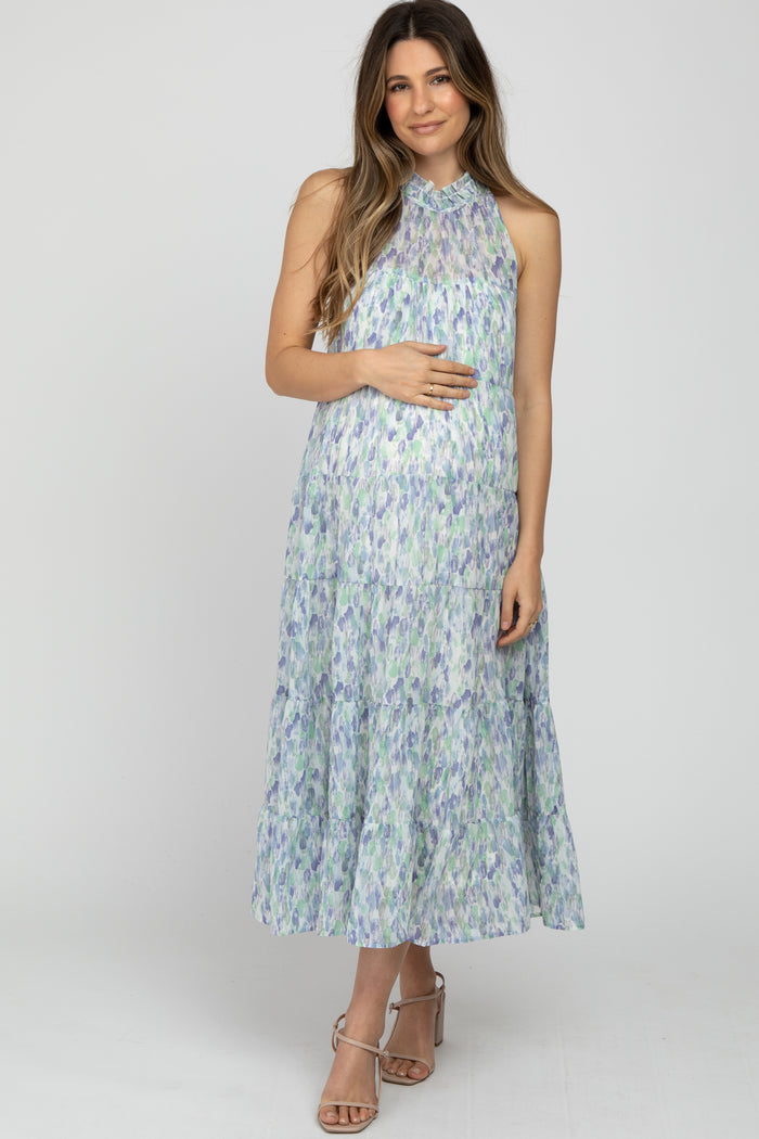 woman wearing a light green and purple floral maternity dress with a halter neck, gently holding her baby bump