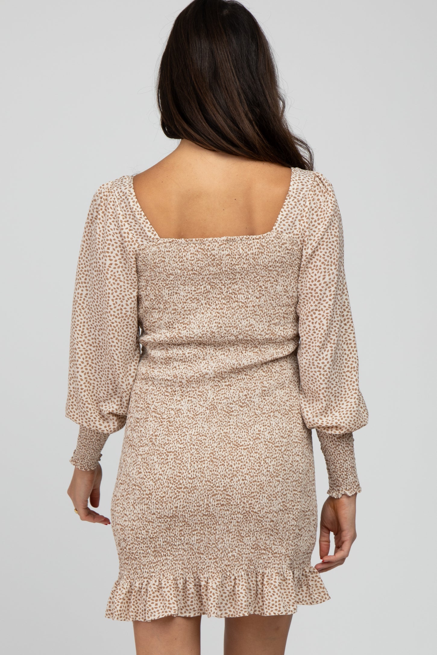 woman wearing a beige floral print mini dress with puff sleeves and a ruffled hem viewed from the back