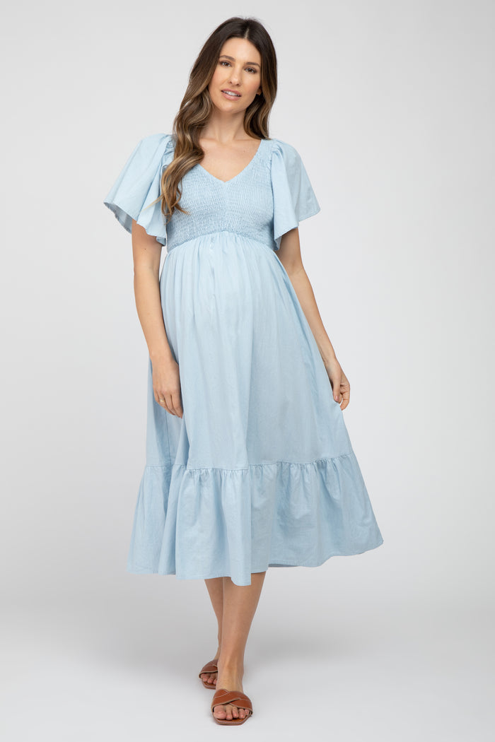 woman wearing a light blue maternity dress with flared sleeves and a tiered hem, showcasing her baby bump